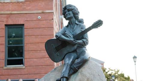 A statue of Dolly Parton sitting on a rock holding a guitar.