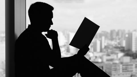 The Silhouette of a man reading against a window