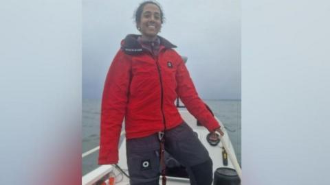 Ananya Prasad smiling as she stands on her boat in the ocean