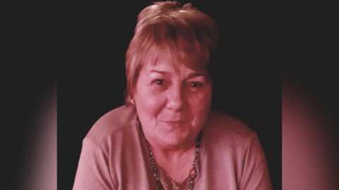 Nora O'Hagan - a woman with short hair looks at the camera. She is wearing a light coloured top and a necklace. The background is dark and there is a pink coloured filter placed over the picture.