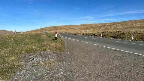 The Mountain Road looking in the northern direction. There is heathland on either side of the carriageway and a clear deep blue sky above.