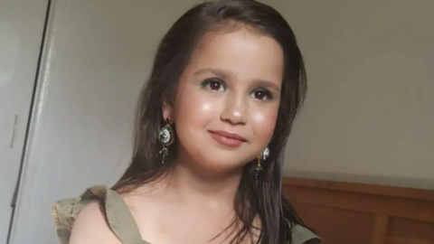 a little girl with long brown hair, wearing make-up and long dangly earrings