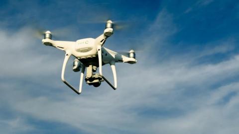 A white drone flying against a blue sky