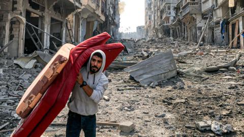 A man walks with mattresses through destruction in the Gaza Strip's Jabalia refugee camp