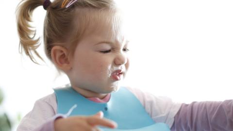 A fussy toddler eating and making a face