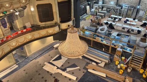 Inside the Jersey Opera House during its recent £13m renovation. A chandelier is hanging from the ceiling. Lots of building materials are scattered on the floor and the venue's stage. 