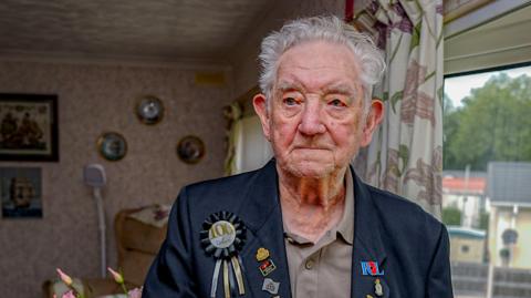 Veteran Reg Draper stood in his home wearing a smart blue blazer and tshirt wearing his war medals 