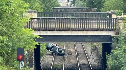 A silver car overturned on railway tracks.