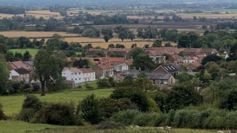 A birdseye view of Bishop Wilton from above. In between hills and greenery, several large buildings can be seen.