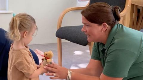 A picture of Chantelle and a child holding a teddy bear. She has a silver bracelet on.