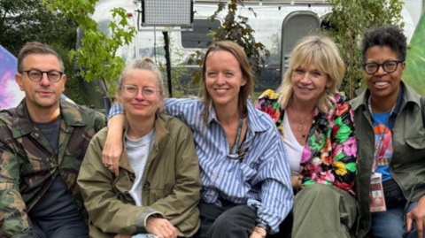 (Left to Right) - Jonathan Rothery, Alison Howe, Emily Eavis, Zoe Ball, Lorna Clarke all sat on a bench backstage at Glastonbury Festival.
