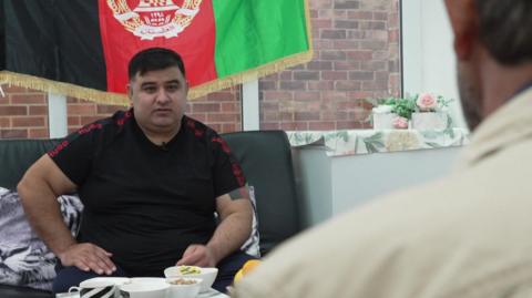 Hamidullah Khyber is sitting with one of the other Afghan refugees, who has his back to the camera.