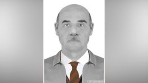 A police image of a man with no hair at the top of his head, with a red tie and a grey anorak and a white shirt.
