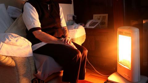 A generic stock photo of an elderly person sitting at home with their electric fire on