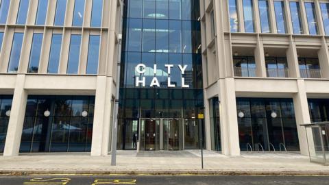 The outside of Sunderland City Hall which is a large building with large rectangle windows with 'City Hall' written in large white letters above the glass entrance.