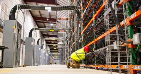 A technician wearing PPE working on racks of equipment in a data center for cryptocurrency mining, cloud services and AI computing in a large, temperature controlled warehouse in a remote location in Stutsman County, North Dakota.