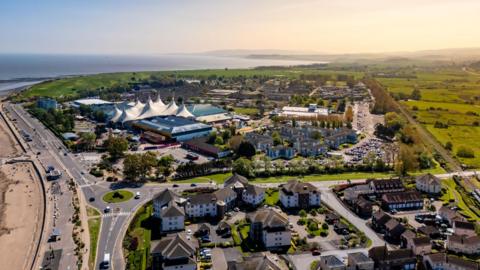 An aerial shot of Minehead in Somerset. It is a sunny day and the distinctive white tent-like structure of Butlins is visible as well as the coastline in the distance