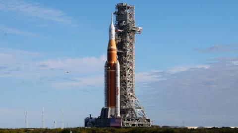 A large rocket stands at a launch pad before a blue sky.