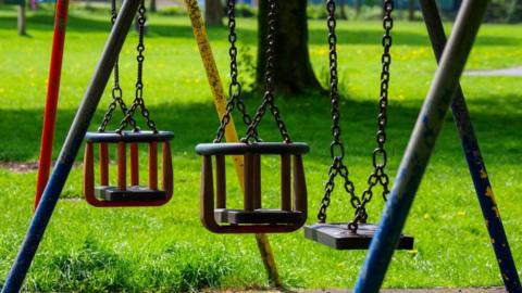 A photograph of three children's swings in a playground.
