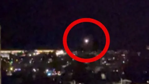 A red circle highlighting a drone flying over the night sky 