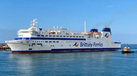 A white ferry with blue tipped chimneys with the words Brittany Ferries on the side arriving in St Peter Port Harbour.