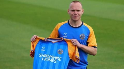 Anthony Scully poses with a Shrewsbury Town home shirt after signing for the club