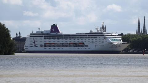 A large cruise ship, which is white, with purple and green markings, is seen docked at a port 