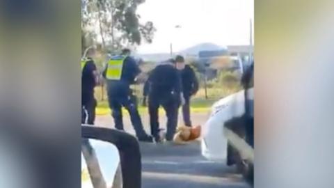 Four police officers stand over the man who is lying on the ground during the arrest