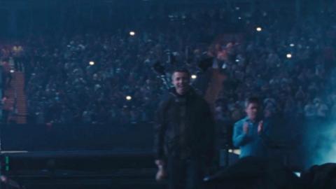 Liam and Noel walking on stage, it is dark and there are phone torches lit in the packed crowd