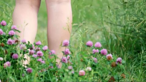A pair of naked legs walking on grass.