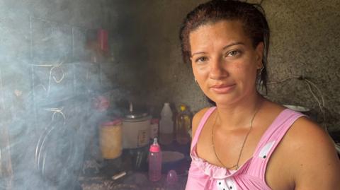 A woman in a pink sundress is seen in her kitchen