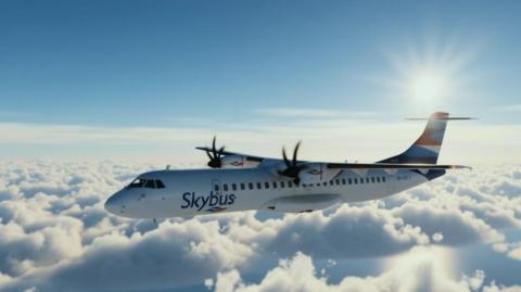 A white plane with blue wings flying above the clouds with 'Skybus' is blue lettering on the side of it.