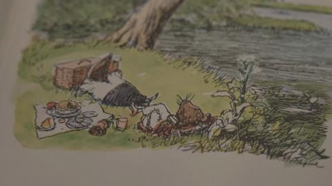 Illustration from Wind in the Willows book shows Mole by the banks of a river relaxing with a picnic beside him.