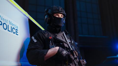 A West Mercia armed police officer wearing a face covering, helmet and holding a gun