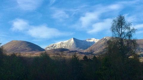 Photograph of a mountain range with some white snow sprinkled on the peaks.  Sunshine fills the skies around it.