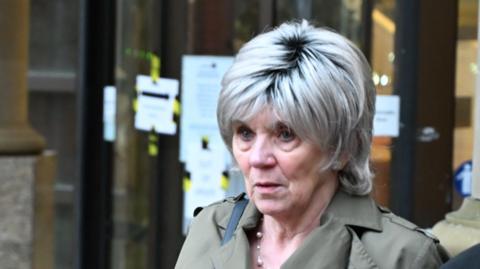 A 77-year-old woman with blonde hair and a green jacket leaves court