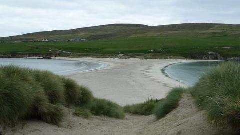 a beach which has water on either side and hills in the background