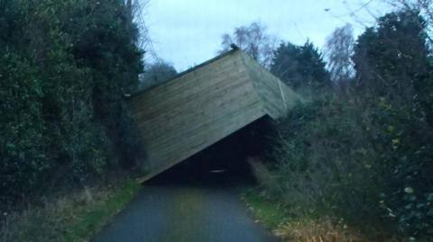 A wooden field shelter in the middle of a single-track country road.