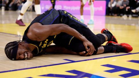 Golden State Warriors forward Jimmy Butler lies on the floor in agony, holding his right knee after tearing his ACL