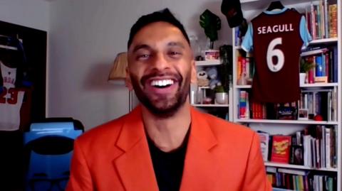 Bobby Seagull, wearing a red jacket, smiles at the camera. 