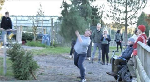 A man in a grey jumper and dark trousers throwing a Christmas tree over his shoulder.