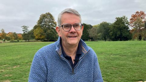 Simon Marsh, Battlefields Trust in a blue quarter zip jumper. He is wearing glasses and standing in the grounds of Delapre Abbey.
