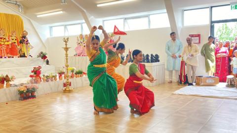 Hindu dancers perform in colourful saris in front of a stage full of religious statues