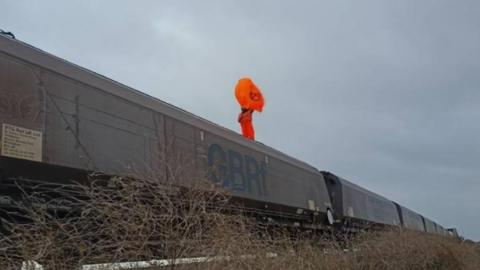 Karen Wildin on top of the train dressed in orange clothing and waving an orange Extinction Rebellion flag