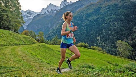 A runner in a coloured top and short races through the backdrop of snow-capped mountains