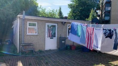 Small property on a single floor with a washing line hung outside holding laundry. The ground is covered in brickwork.