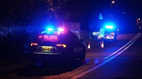 Two police cars at the side of the road with their blue lights on