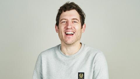 Elis James smiling in a white t-shirt