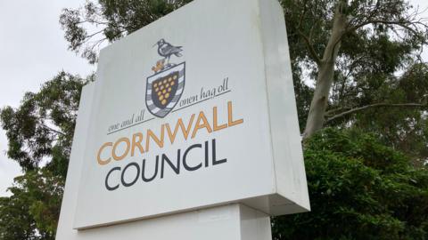 Cornwall Council sign in front of some trees. The sign is white and square with yellow and black writing. 