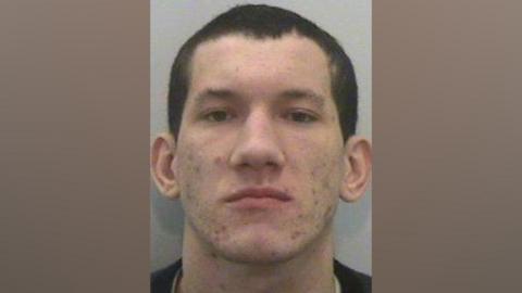 Custody shot of Anthony Ellis from 2013. He has short cropped dark hair and acne.
